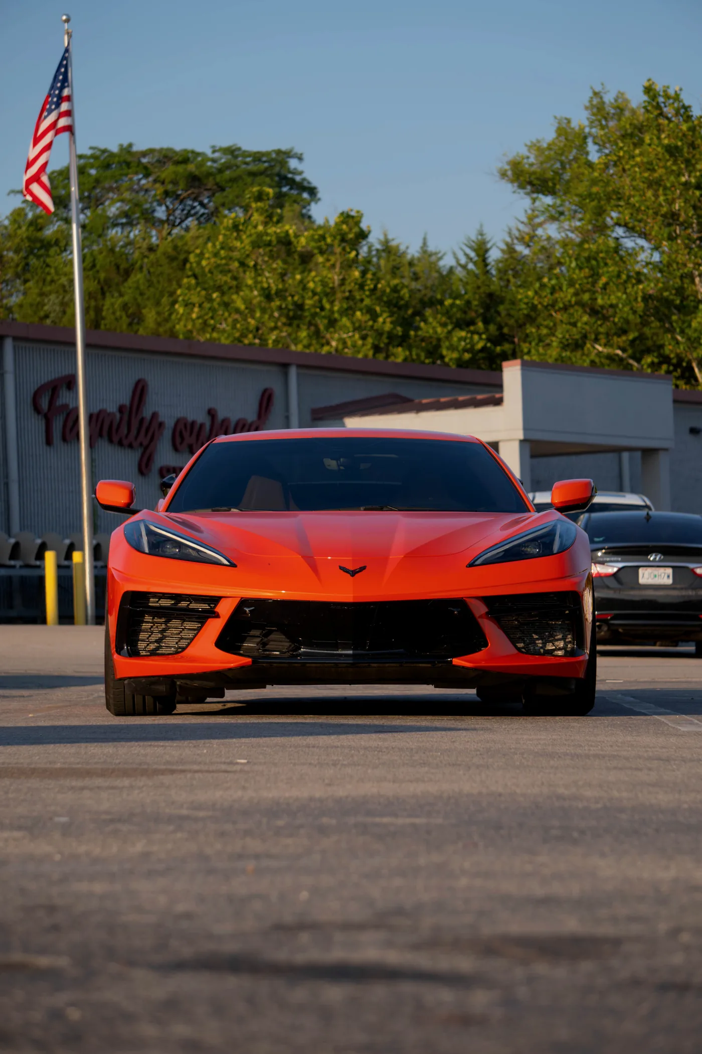 Chevrolet Corvette C8 head-on at a dealership, orange paint, American flag flying