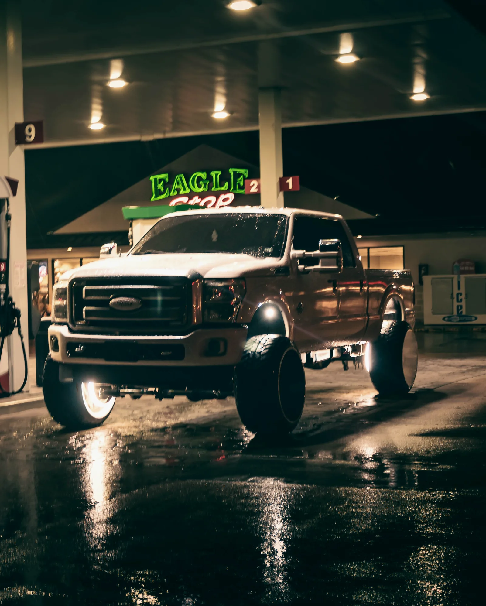 Lifted Ford Super Duty truck under gas station lights at night in the rain